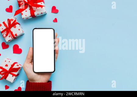 Woman hand holding mobile phone with blank screen on colored background with hearts, valentine day concept top view flat lay. Stock Photo