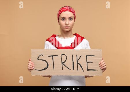 Beautiful woman holding cardboard banner with word Strike on beige background Stock Photo