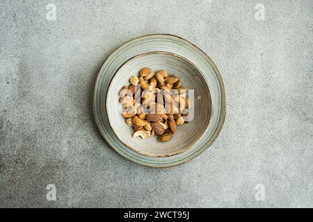 A ceramic bowl filled with mixed nuts is centered on a textured grey surface, offering a minimalist and organic aesthetic Stock Photo