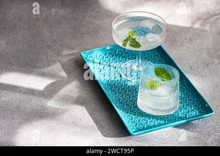Two stylish cocktail glasses on a blue textured serving tray, adorned with mint leaves, set against a soft shadowy background Stock Photo
