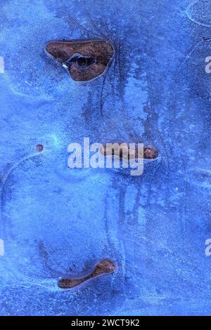 Icy textures with embedded stones, forming a natural mosaic on the frozen ground during early winter Stock Photo