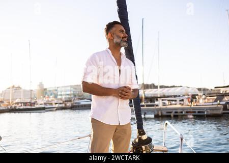 Smiling bearded male in white shirt looking away yacht against blue sea and sky Stock Photo