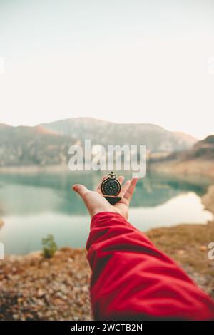 Anonymous hand holding a compass with a scenic lake and mountains in the background symbolizing guidance and exploration Stock Photo