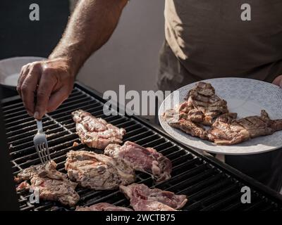 From above of unrecognizable person putting pieces of grilled meat on plate with fork from barbecue grill Stock Photo