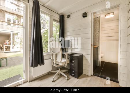 Computer on work desk in small backyard shed at contemporary house with door and bathroom Stock Photo