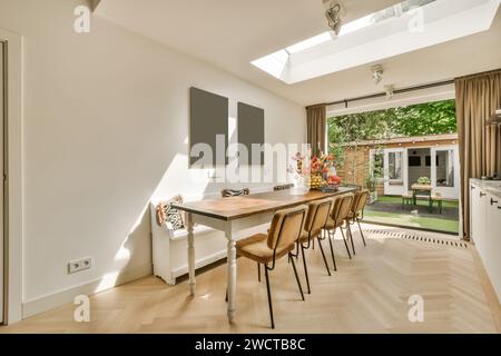 Long wooden dining table and chairs arranged by large window in dining room at modern house overlooking backyard Stock Photo