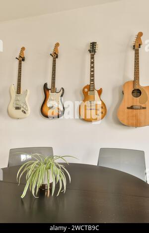 Round black wooden table and chairs in dining room of luxurious apartment with guitars hanging on white wall Stock Photo