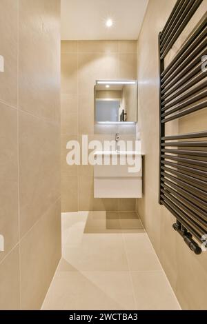 Sink and mirror in small illuminated bathroom at contemporary apartment with black radiator on tiled wall Stock Photo