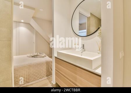 A chic bathroom design featuring a sleek sink, round mirror, and a view of the adjoining bedroom. Stock Photo