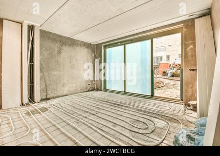 An underfloor heating system laid out on a concrete floor in a room under construction, with large windows and unfinished walls. Stock Photo