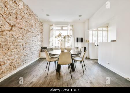 A contemporary dining space featuring a stylish table set, exposed brick feature wall, wood flooring, and ample natural light from the large windows. Stock Photo