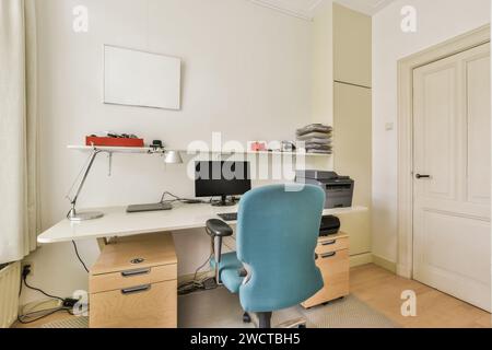 A neatly organized home office interior featuring a white desk with a desktop computer, office supplies, and a comfortable blue office chair. Stock Photo