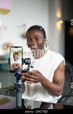 Cheerful black man records a skincare tutorial using a smartphone and gimbal with a modern interior background Stock Photo