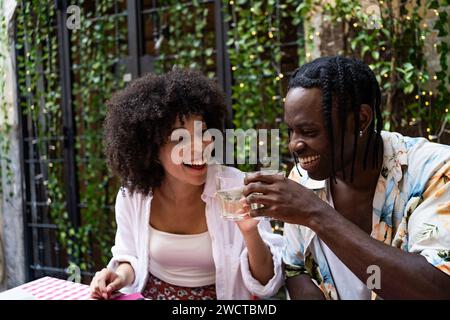 Two friends laugh over drinks in a lively garden cafe enjoying a cheerful moment together Stock Photo