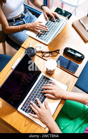 From above view of unrecognizable colleagues using laptops in a cafe, with smartphones and coffee cups on the table, showcasing a collaborative remote Stock Photo