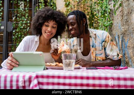 Ethnic friends share a meal and engaging interaction with a digital tablet at a vibrant cafe in Rome Stock Photo
