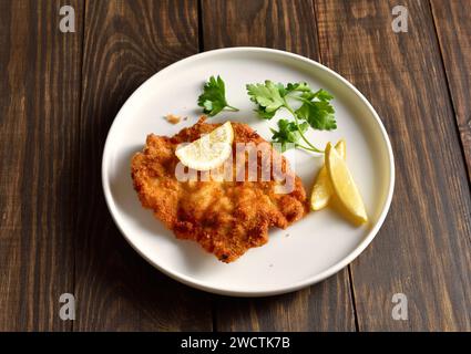 Pork schnitzel with lemon and leaves of parsley on white plate over wooden background. Close up view Stock Photo