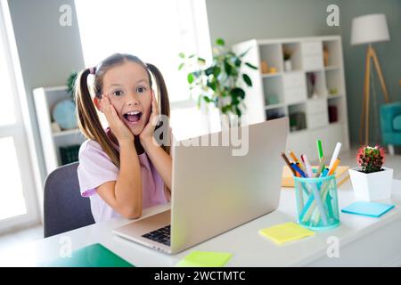 Photo of positive astonished small girl sit chair open mouth unbelievable perfect test grade apartment indoors Stock Photo