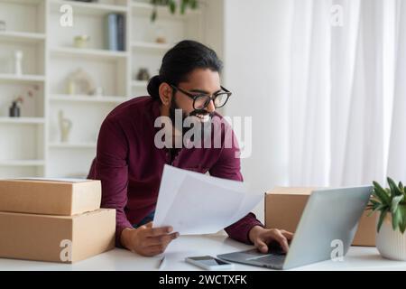 Smiling indian businessman analyzing documents and using laptop in home office Stock Photo