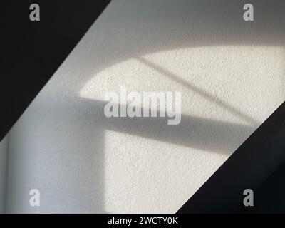 Play of light and shadow on a white textured wall, creating an abstract geometric pattern. Stock Photo