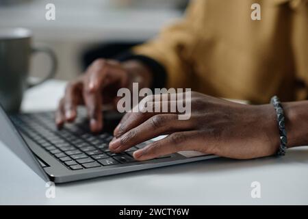 Closeup of hands of african american man typing on laptop keyboard while sitting at desk Stock Photo