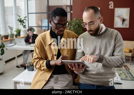 Biracial male workers looking at digital tablet screen and discussing business project Stock Photo