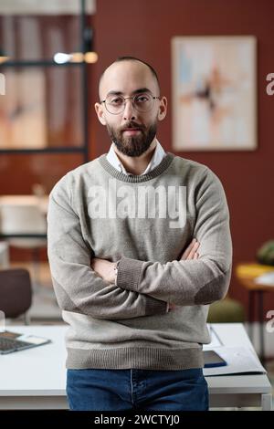 Man confidently standing with his arms crossed posing by his workplace in office Stock Photo