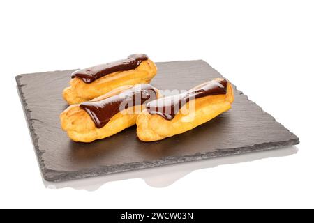 Three sweet chocolate eclairs on slate stone, close-up isolated on white background. Stock Photo