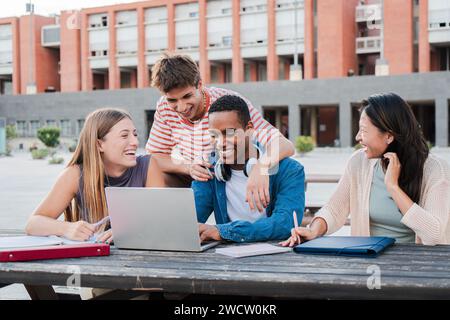 Group of young classmates studying together and preparing a exam using a laptop, browsing on internet at university campus. Teenage students smiling and doing the homeworks with a notepad computer. High quality photo Stock Photo