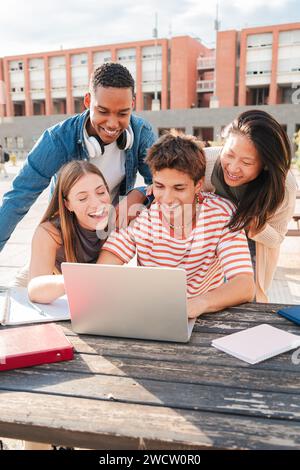 Vertical. Group of young classmates studying together and preparing a exam using a laptop, browsing on internet at university campus. Teenage students smiling and doing the homeworks with a computer. High quality photo Stock Photo