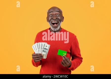 Overjoyed elderly African American man holding cash in one hand and a green credit card Stock Photo