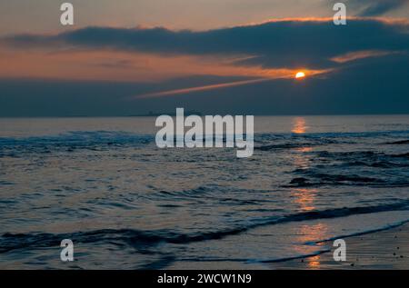 Looking out to sea from Bamburgh Beach Coast  early morning in March with the setting sun and the orange path across the North Sea Stock Photo