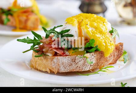 Breakfast. Sandwich with ham, poached egg, onion and arugula in a plate on a light background Stock Photo