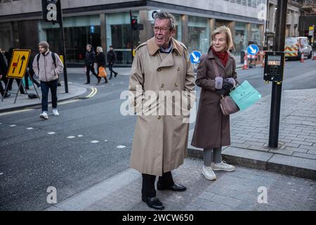 A man in a winter raincoat stands at a pedestrian crossing checking the road is clear to cross, Piccadilly, London, England, UK Stock Photo