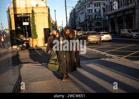 A tramp wearing a thick winter overcoat walks down Piccadilly towards Marble Arch, London, England, United Kingdom Stock Photo