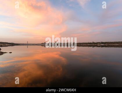 Cityscape during sunset on the bank of a wide river in which the sky is reflected. Background Stock Photo