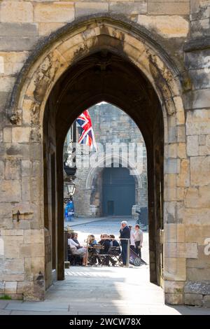 Lincoln, Lincolnshire, England. View through 14th century Exchequer Gate to customers relaxing outside a pub in Castle Square. Stock Photo