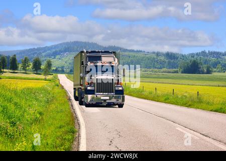 Classic American truck semi trailer on rural road through beautiful summer landscape on a sunny day. Stock Photo