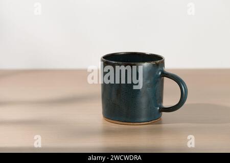 A dark blue ceramic mug in Japanese style is placed on a wooden table with a white background. Stock Photo