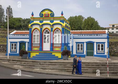 Portugal, Azores archipelago, Terceira island, Praia da Vitoria, couple dressed in their Sunday best in front of the Imperio do Divino Espirito Santo da Caridade, a multicolored chapel dedicated to the holy spirit Stock Photo