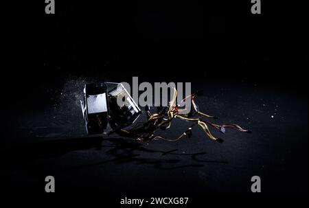 Male hands hitting hard PC power supply on the floor, demolishing and breaking PSU, isolated on a black background, slow motion shot. Computer Stock Photo