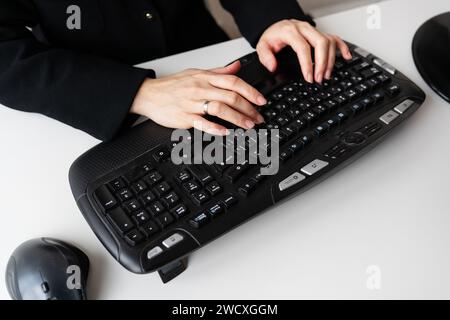 A girl in a black outfit typing on a full-sized black keyboard with a mouse. The keyboard has various function keys and multimedia buttons visible Stock Photo