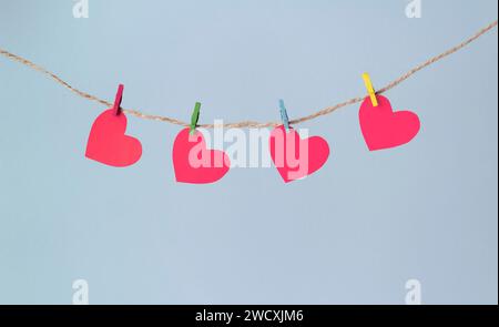 Paper hearts hang on clothespins on a rope on a pastel blue background. Valentine's day concept. Stock Photo