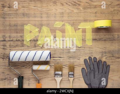 Painting tools on a wooden background with the word Paint made from masking tape. House or apartment renovation. Stock Photo