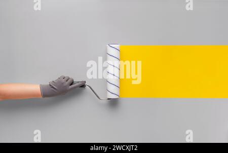 Girl in a glove paints a yellow strip with a roller on a gray wall. Creative renovation concept. Stock Photo