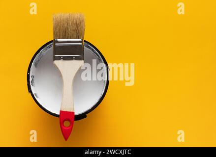 Paint brush on top of can with white paint on a yellow background. Renovation concept. Stock Photo