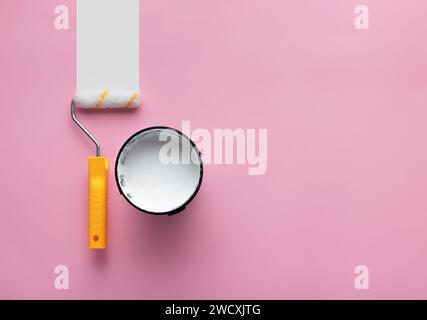 Can of white paint and roller with white strip of paint on a pink background with copy space. Stock Photo