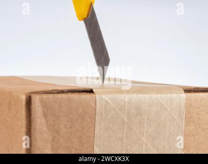 Opening cardboard box with yellow stationery knife. Close up. Stock Photo