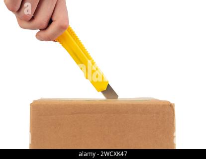 Opening cardboard box with yellow stationery knife. Close up. Side view. Stock Photo