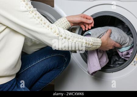 mom puts the baby's clothes in the washing machine. Stock Photo